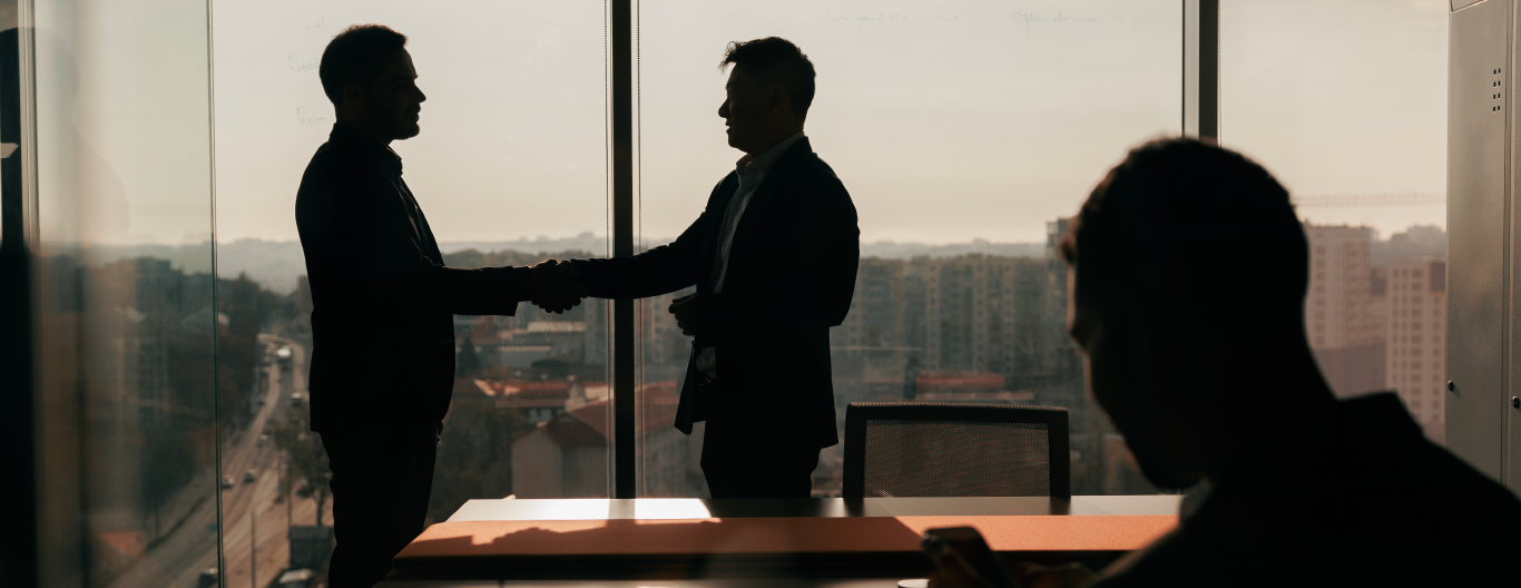 3 personas en una oficina, 2 de ellas de pie estrechándo las manos