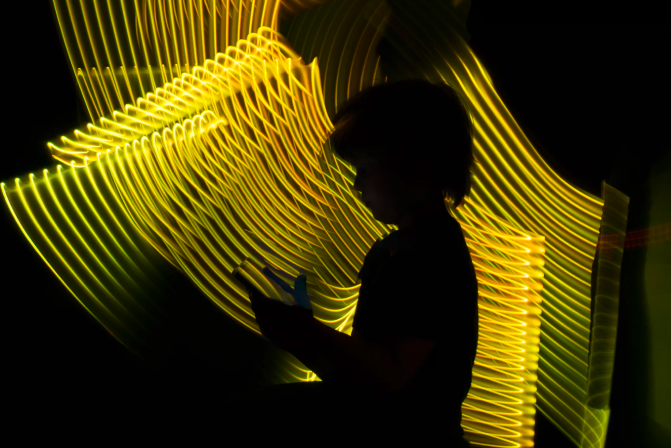 silueta de persona en negro con teléfono móbil en la mano y al fondo líneas ondeadas amarillas