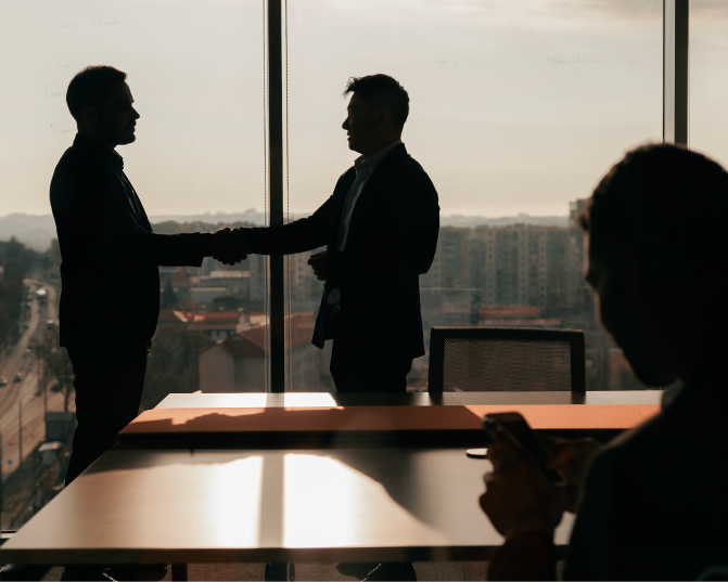 2 personas de pie en una oficina estrechandose las manos y otra persona sentada